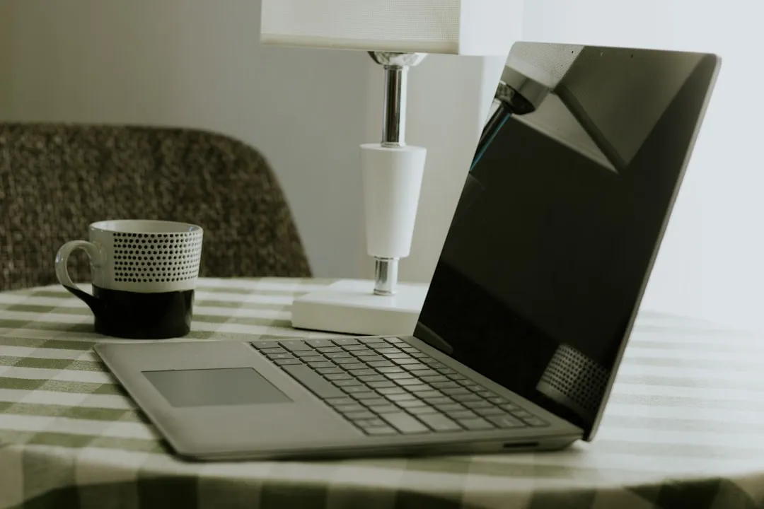 チェック柄のテーブルクロスの上に開いたノートパソコンとマグカップ。
