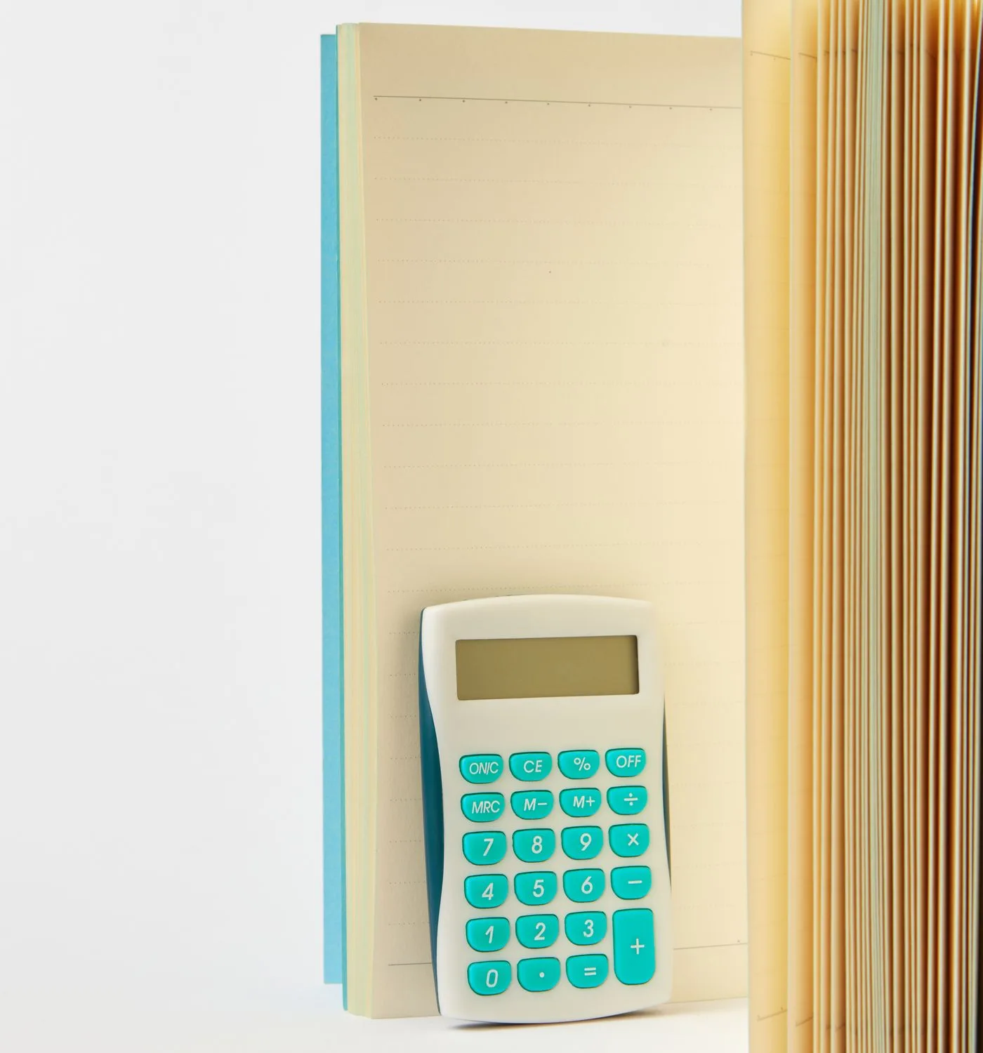 薄い青の罫線ノートに立てかけられた、ターコイズ色のボタンの電卓。