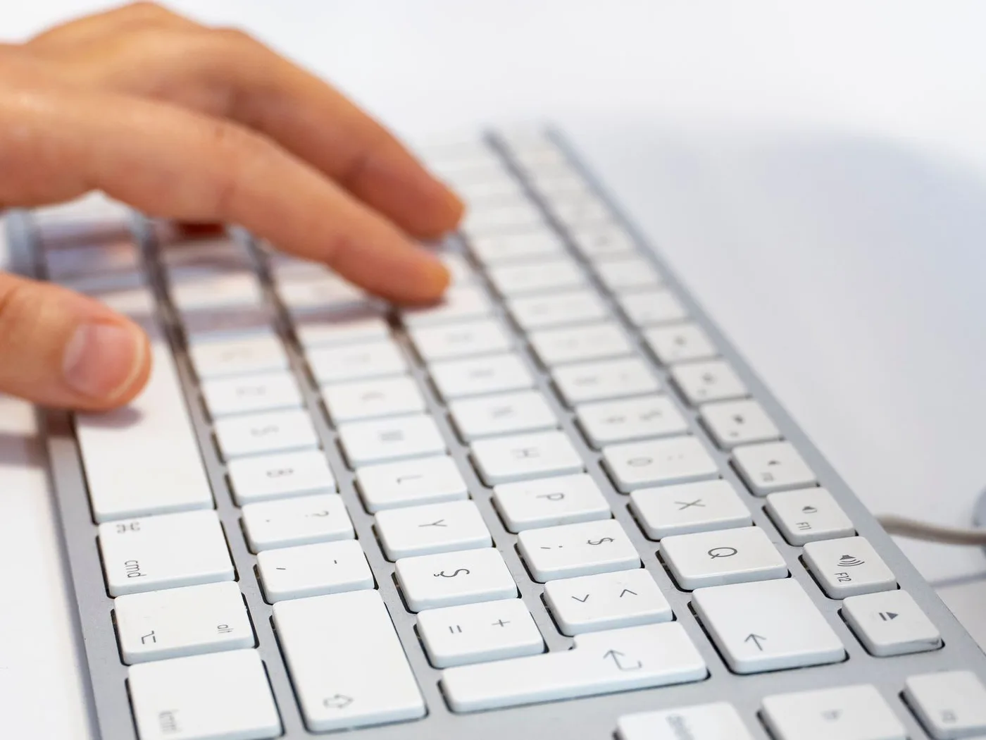 白いキーボードに指を置いてタイピングしている手元。