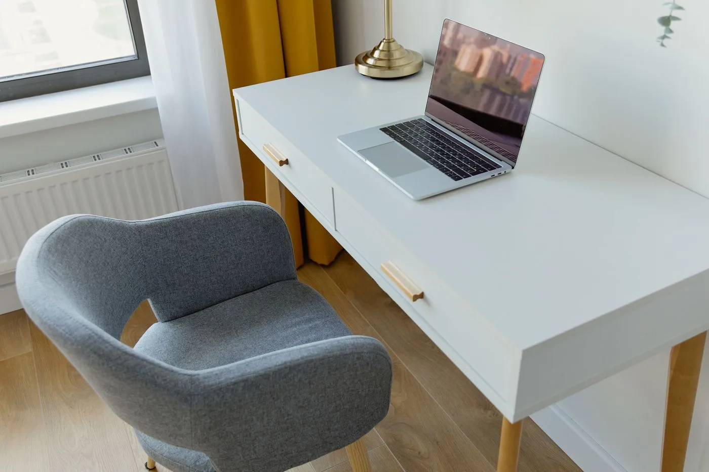 明るい部屋に置かれた白い机とノートパソコン、グレーの椅子。