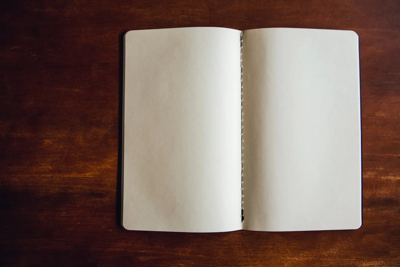 濃い色の木の机に、何も書かれていないノートが見開きで置かれている。