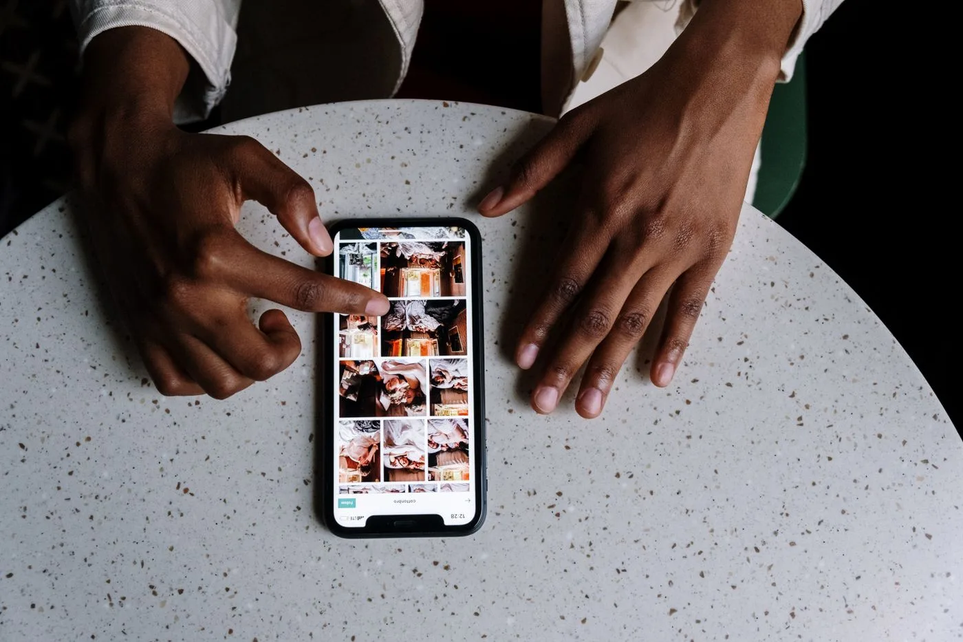 丸いテーブルに置かれたスマートフォンの画面を、指で操作している手元。